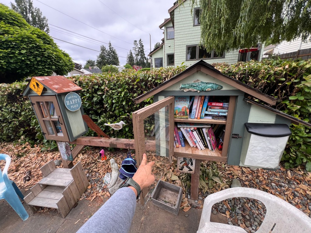 A miniature library structure labeled 'Happy Place' with open shelves displaying a variety of books, surrounded by greenery and outdoor furniture.