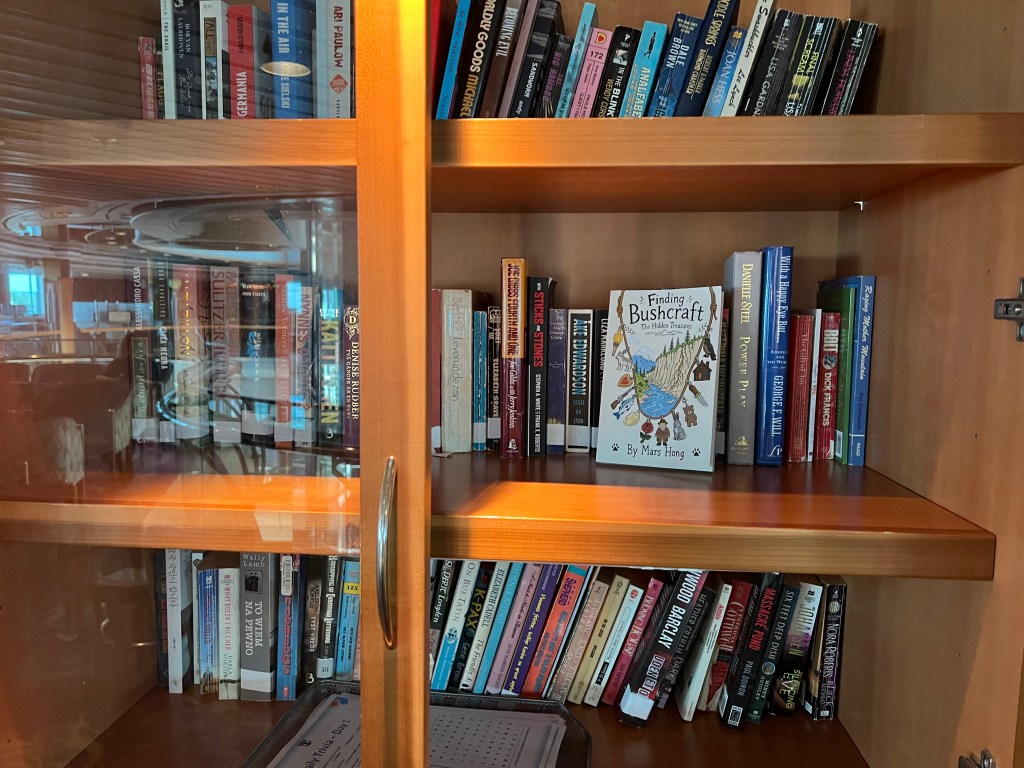 A wooden bookshelf displaying a variety of books, with 'Finding Bushcraft' prominently featured in the center. The shelf contains both fiction and non-fiction titles.